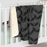 Grey blanket with bat print and also showing white soft underside hung over the side of cot railings
