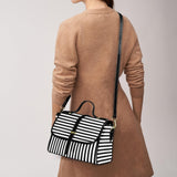 Person wearing a brown coat with a black and white striped bag over their shoulder on a plain background