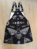 Black celestial witchy style shortalls dungaree overalls with gray moth and moon phase pattern on a white background by Alternawear clothing back lying on the floor