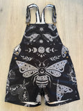 Black celestial witchy style shortalls dungaree overalls with gray moth and moon phase pattern on a white background by Alternawear clothing front lying on floor