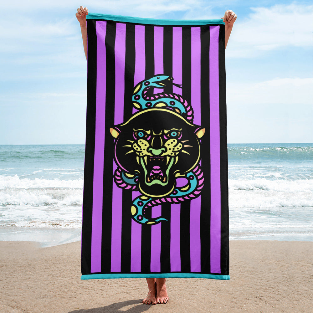 Purple and black striped towel with teal detail and snake and banter print, being held up in the corners vertically on a beach