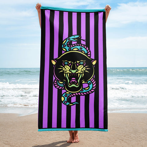 Purple and black striped towel with teal detail and snake and banter print, being held up in the corners vertically on a beach