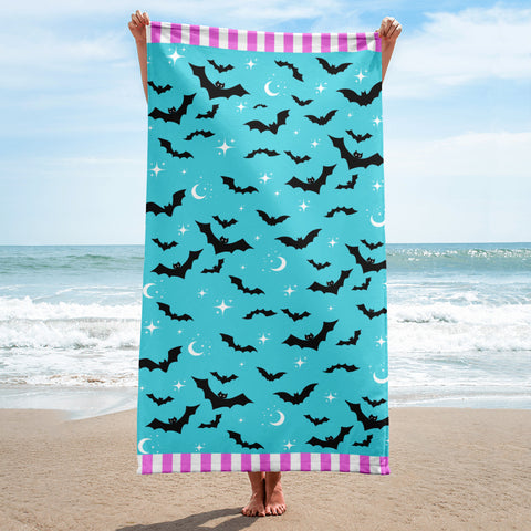 blue bat print gothic beach towel being held up in the air by the sea